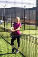 Lycklig kvinna paddla tennis spelare under öva på utomhus- domstol ser på kamera. kopia Plats. foto