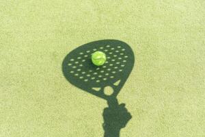 skugga av en padel racket med en gul boll på de grön gräs. foto