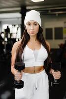 ung passa kvinna praktiserande hantel Tryck medan stående i de Gym. smal kvinna i sportkläder övningar med vikter i en Gym foto