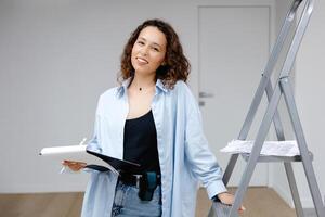 en ung Söt flicka designer håller dokument medan stående på henne arbetsplats. lägenhet renovering och design begrepp foto