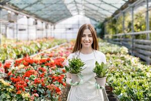 kvinna innehar en pott av blommor i henne händer, växande växter för försäljning, växt som en gåva, blommor i en växthus, inlagd växt. foto