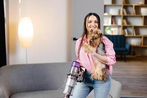 kvinna med Vakuum rengöringsmedel och hund i henne hand dammsugning i de levande rum. foto
