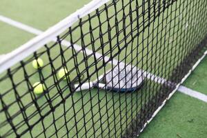 blå padel racket och gul bollar placerad på domstol nära netto på solig dag foto