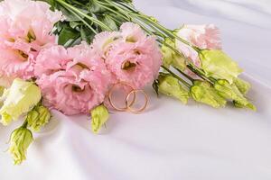 två guld klassisk bröllop ringar på en vit satin bakgrund med färsk rosa austoma blommor. en kopia Plats. vykort. inbjudan. omslag foto