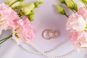 två guld klassisk bröllop ringar på en vit satin bakgrund med färsk rosa austoma blommor. en kopia Plats. vykort. inbjudan. omslag. foto