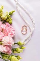 skön bröllop vertikal bakgrund med två guld ringar, pärla pärlor, rosa austoma blommor. topp se. hälsning kort, inbjudan, mockup. foto