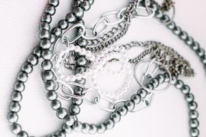 en halsband av grå pärlor med kedja dekorationer på en vit estetisk bakgrund. foto