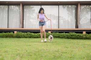 Lycklig asiatisk kvinna spelar med söt smart mops valp hund i de bakgård foto