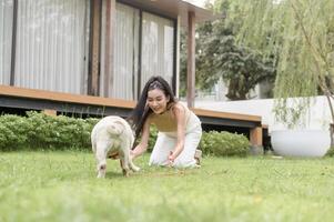 Lycklig asiatisk kvinna spelar med söt smart mops valp hund i de bakgård foto