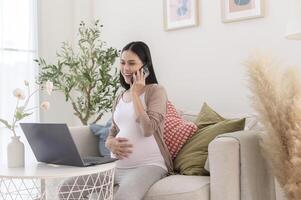 gravid kvinna arbetssätt på bärbar dator och smart telefon i de levande rum på Hem foto