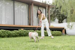 Lycklig asiatisk kvinna spelar med söt smart mops valp hund i de bakgård foto