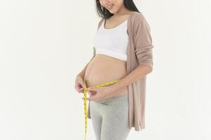 gravid kvinna använder sig av mätning tejp till kolla upp storlek av mage graviditet och bebis utveckling foto