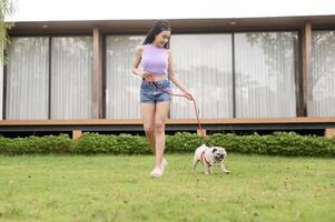 Lycklig asiatisk kvinna spelar med söt smart mops valp hund i de bakgård foto