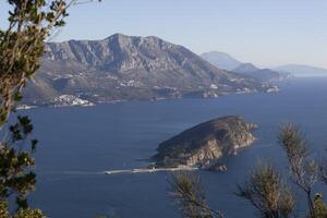 vinter- hav färgrik landskap med blå vatten av de adriatisk hav och de ö av st. nikola nära de stad av budva i montenegro. se från ovan genom de träd. horisontell foto