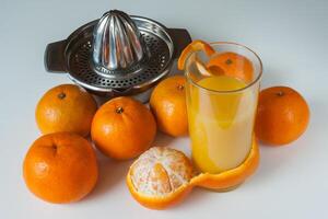 glas av friska färsk juice av mandariner och manuell juicepress på vit bakgrund foto