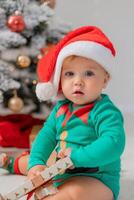 bebis i jul gnome kostym öppnas gåvor nära jul träd. Produkter för barn och högtider foto