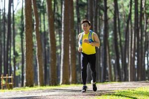 asiatisk spår löpare är löpning utomhus- i de tall skog smuts väg med vatten ryggsäck för övning aktiviteter Träning till lopp i de ultra maraton till uppnå friska livsstil och kondition foto