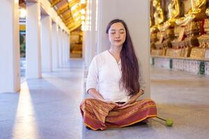 buddist asiatisk kvinna i traditionell trasa är håller på med mindfulness meditation i buddist tempel för fred och lugn religion öva foto