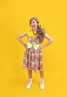 asiatisk hippie kvinna klänning i 80s årgång mode med färgrik retro Kläder medan Framställ isolerat på gul bakgrund för fint utrusta fest och pop- kultur begrepp foto