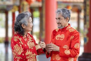 asiatisk äktenskap senior par i Cheongsam qipao klänning är framställning en önskar till förfäder Gud inuti kinesisk buddist tempel under lunar ny år för bäst önskar välsignelse och Bra tur foto