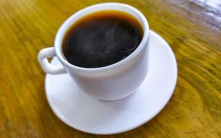 vit kopp av svart americano kaffe på en trä- tabell. foto