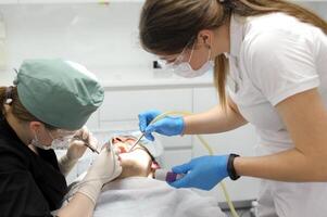 tandvård läkare behandlar en tand i en man patient kvinnor i masker på dem steril handskar smart Kolla på modern teknologi dental behandling tand extraktion ont tänder rengöring tänder dental kontor foto