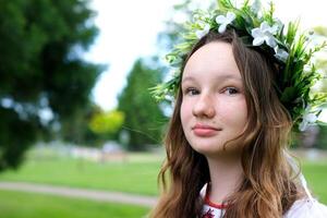 skön söt ung flicka tonåring ser på de kamera leende på henne ukrainska kläder och en skön krans med vit blommor natur lugn där är en plats för text foto