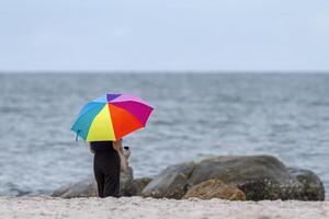 kvinna med regnbåge paraply på en molnig strand foto