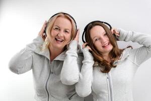 kvinna och flicka mor och dotter lyssnande till musik på hörlurar dans i de samma kläder två generationer ömsesidig förståelse vänner på en vit bakgrund dans flicka sång foto