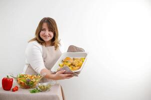 banderoller reklam tjänande mat värdinna kokta utsökt kött vegetabiliska sallad kvinna leende utseende in i ram Plats för text på vit bakgrund håll bakning ark med ugn vantar skön knubbig flicka foto