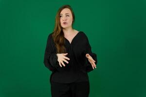 kvinna i en svart Byxor kostym gestikulerar med henne händer med henne fingrar spridning ut på grön bakgrund visar talande med henne mun lite öppen kommunikation lärare reklam chef företag foto