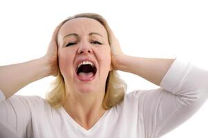 kvinna är skrikande och beläggning hugga öron med händer stänga horisontell studio Foto av en rödhårig kvinna skrikande högt klämmer fast henne huvud från chock.