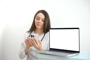 ung kvinna läkare ser in i de telefon Nästa till en bärbar dator med en vit skärm tömma Plats reklam medicinsk teknologi nätverk modern digital kirurg, sjuksköterska, apotek med stetoskop foto
