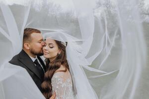 en stilig och eleganta brudgum omfamnar hans brud i en vit klänning under henne slöja foto