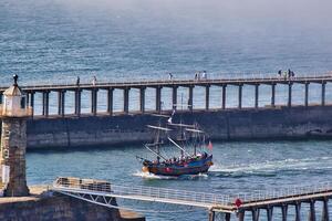 historisk segling fartyg i hamn med pir och fyr i whitby, norr yorkshire foto