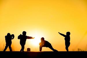 barn siluett leker kul med många vänner och spelar mot solnedgången foto