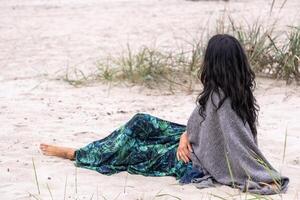 kontemplativ kvinna Sammanträde på de strand, henne blick förlorat i de horisont, förkroppsligar en ögonblick av fredlig reflexion och emotionell balans i medelåldern, som väl som avkopplande. foto