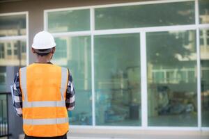 Bakom de scener förman bär reflekterande väst och hård hatt inspekterar konstruktion webbplats till säkerställa konstruktion möter teknik lagets design planer och för de skönhet och säkerhet av invånare. foto