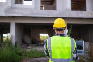 Bakom de scener förman bär reflekterande väst och hård hatt inspekterar konstruktion webbplats till säkerställa konstruktion möter teknik lagets design planer och för de skönhet och säkerhet av invånare. foto