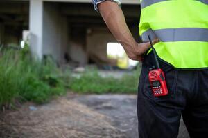 Bakom de scener förman bär reflekterande väst och hård hatt inspekterar konstruktion webbplats till säkerställa konstruktion möter teknik lagets design planer och för de skönhet och säkerhet av invånare. foto