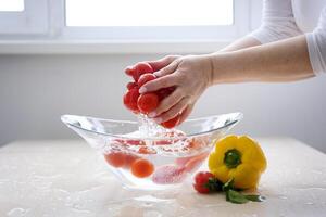 super långsam rörelse skott av flygande färsk tomater med vatten stänk på vit bakgrund vatten i kök i morgon- under kran. framställning grönsaker för framställning utsökt veggie sallad på Hem. foto
