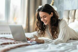 kvinna om i säng använder sig av bärbar dator foto