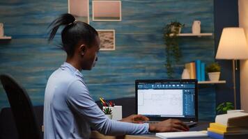 afrikansk frilansare analyserar digital blå grafik kontroll projekt av företag ser på bärbar dator Sammanträde på skrivbord i levande rum kontor sent på natt över tid. upptagen svart anställd använder sig av modern teknologi foto