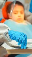 medicinsk team arbetssätt med steriliseras verktyg bär ansikte skydda, overall kostym, mask och handskar under coronavirus utbrott i ny vanligt stomatologisk klinik. tandläkare behandla tänder av liten flicka foto
