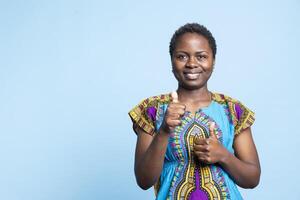 afrikansk amerikan kvinna som visar tummen upp tecken och leende på kamera, presenter avtal på något och känsla nöjd. positiv glad vuxen ger tycka om och visar godkännande med Bra symbol. foto