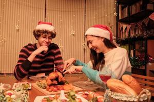 ett ungt par njuter av att äta vid bordet med specialmat, flickvän skära rostad kalkon i hemmets matsal, dekorerad med prydnadsföremål, julfestival och nyårsfest. foto