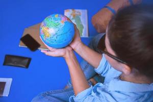 turistplaneringssemester med hjälp av världskartan med andra resetillbehör runt om. kvinna resenär med resväska på blå färg bakgrund. flicka med en boll världen i handen. reseryggsäck foto