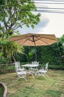 vit tabell med stolar och paraply i de trädgård på bakgård foto