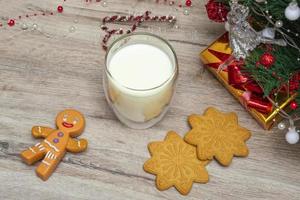 julmjölk och pepparkakor till tomten. ett stort glas med mjölk och juldekorationer. foto av en juldrink på en träbakgrund. närbild