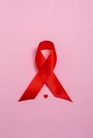 röd aids medvetenhet band och hjärta på rosa bakgrund. närbild, kopiera utrymme. vertikalt foto